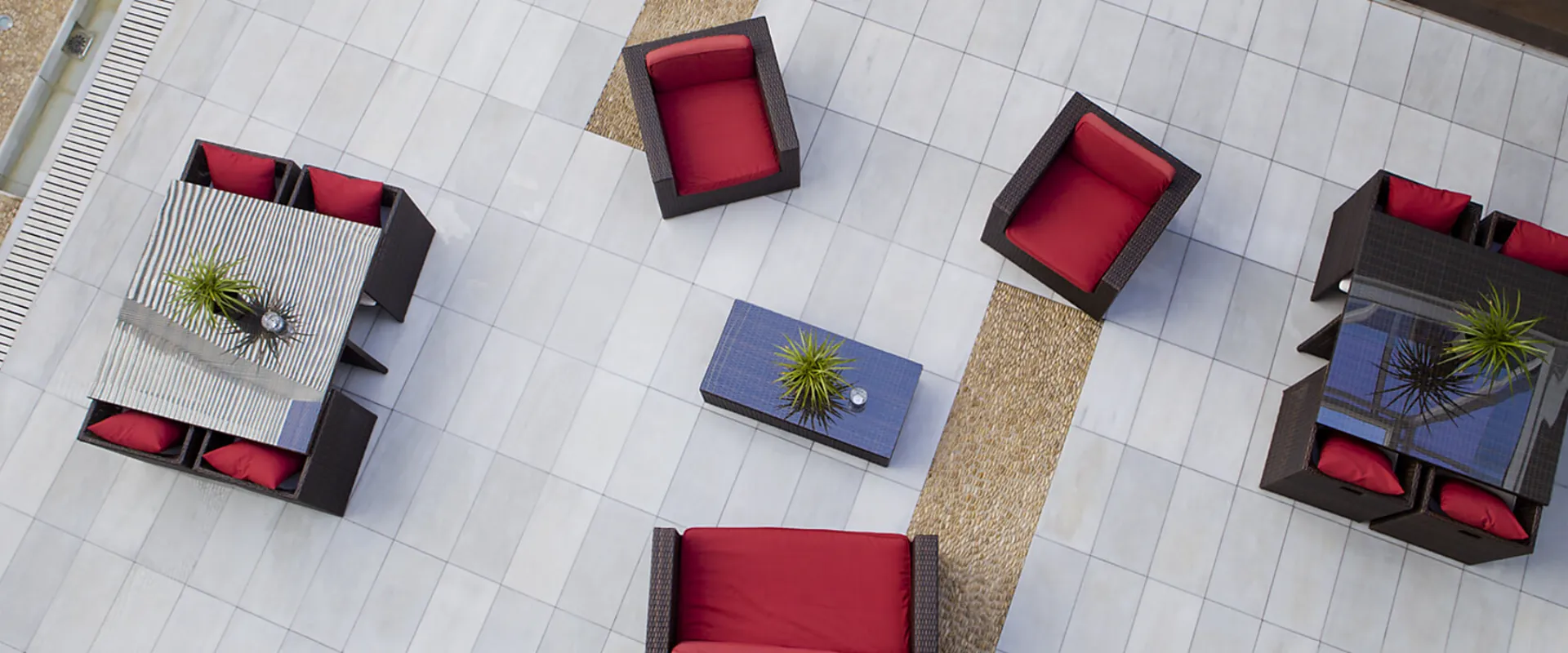 Muebles de exterior con cojines rojos y mesas decoradas con plantas sobre suelo blanco cuadriculado.