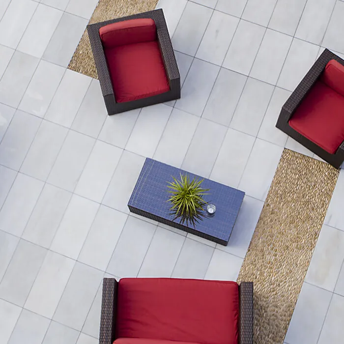 Muebles de exterior con cojines rojos sobre un suelo de baldosas claras, vistos desde arriba.