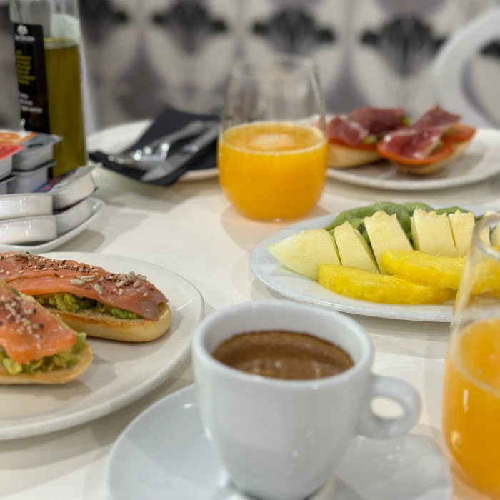 Desayuno con caf&eacute;, jugo de naranja, tostadas con salm&oacute;n y aguacate, y fruta variada.