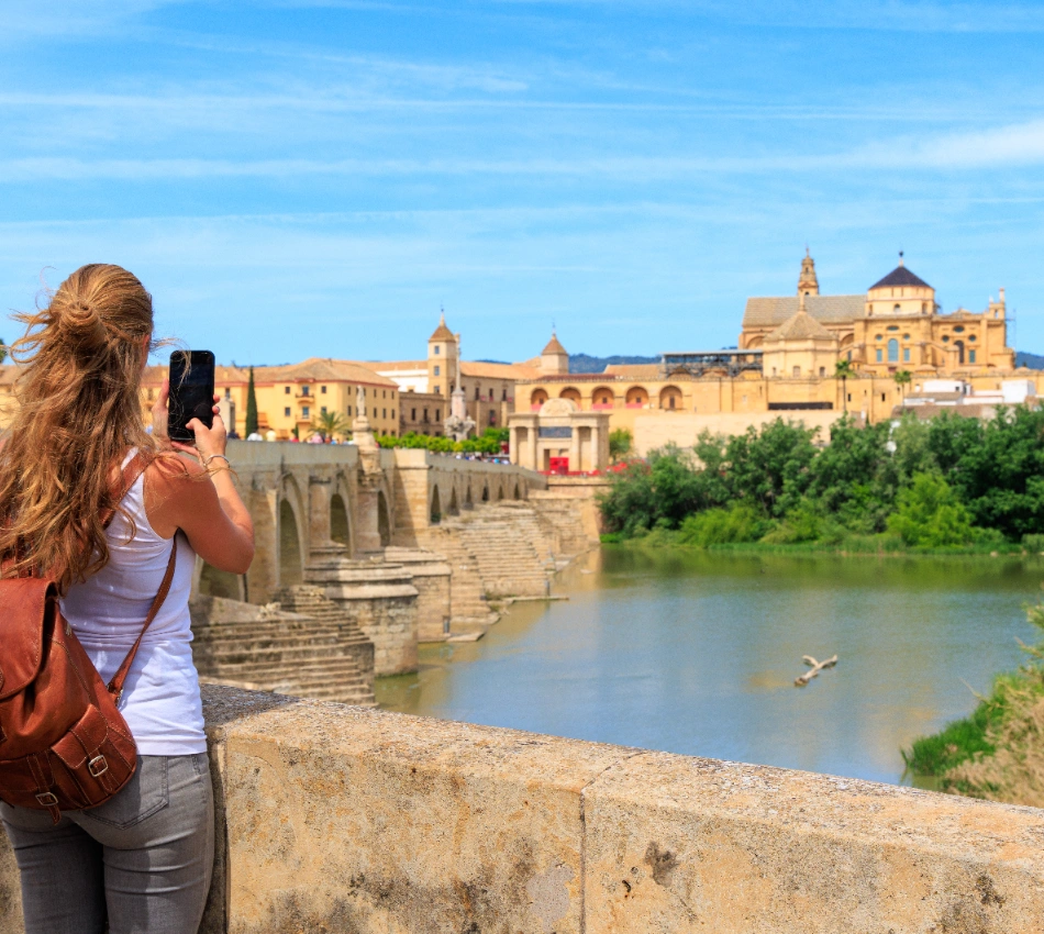 Mujer tomando foto del Puente Romano y la Mezquita en C&oacute;rdoba en un d&iacute;a soleado.