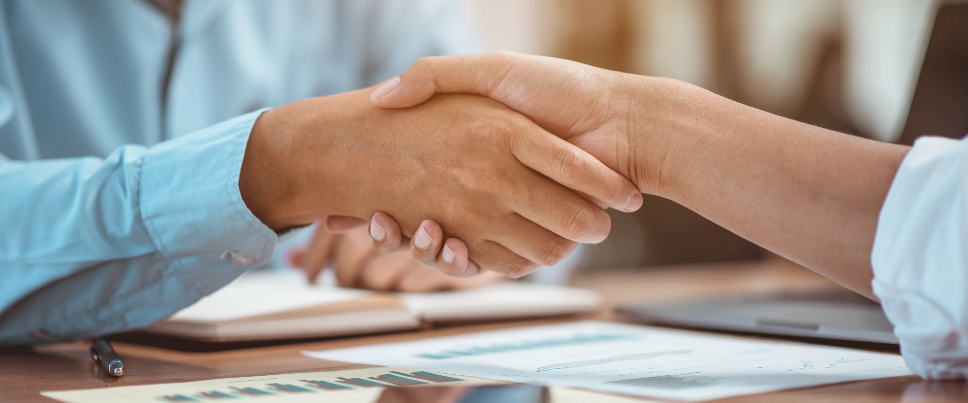 Dos personas d&aacute;ndose la mano sobre documentos en una mesa.
