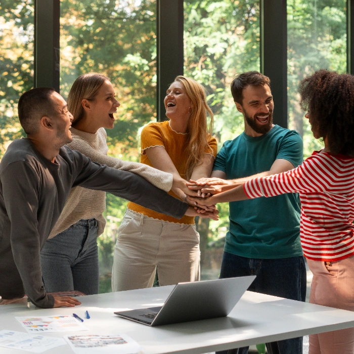Grupo de personas felices juntando las manos en una oficina luminosa con ventanas grandes.