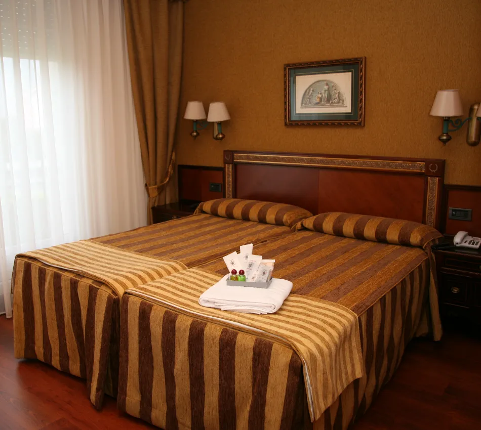 Habitaci&oacute;n de hotel con dos camas, iluminaci&oacute;n c&aacute;lida y decoraci&oacute;n en tonos marrones y dorados.
