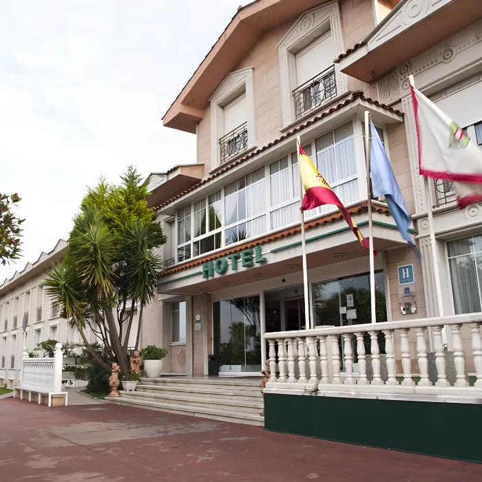 Entrada de un hotel con banderas y una fachada elegante bajo un cielo parcialmente nublado.