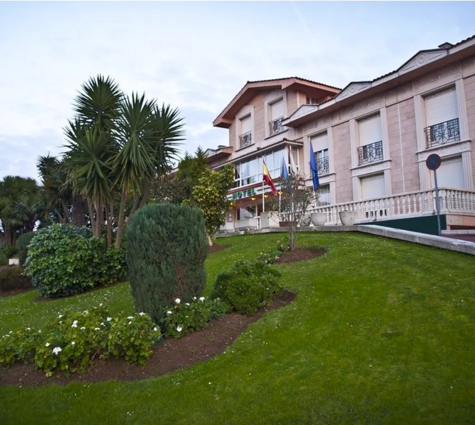 Edificio de hotel en pendiente verde con jardines y palmeras, cielo despejado al fondo.
