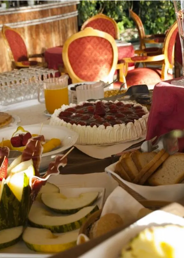 Una mesa con pastel de fresas, mel&oacute;n con jam&oacute;n, pan y jugo de naranja en un restaurante elegante.