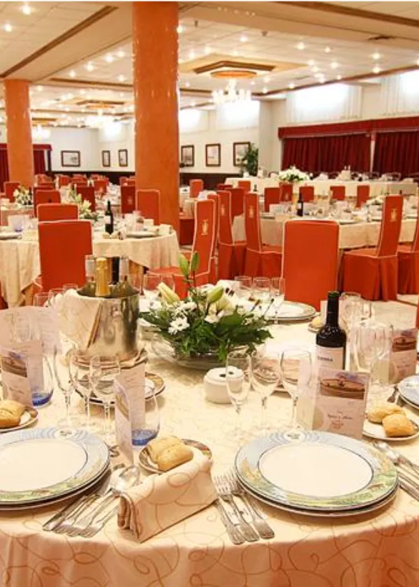 Sal&oacute;n de banquetes con mesas redondas, sillas naranjas y decoraciones florales elegantes.