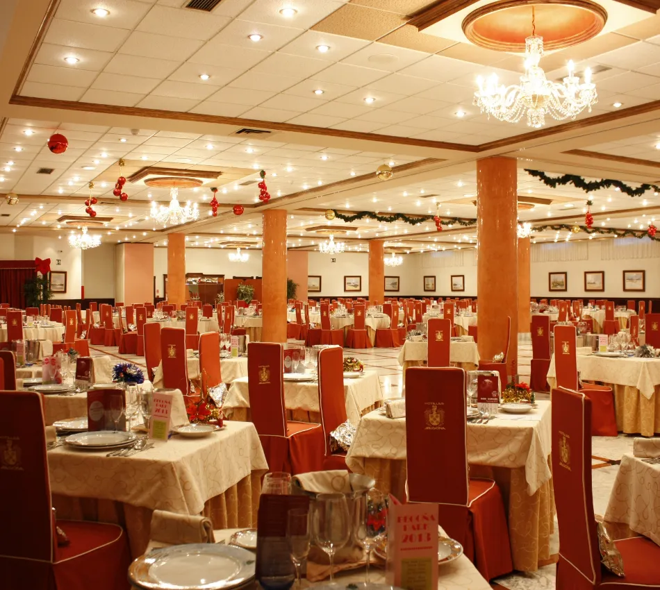 Sal&oacute;n de banquetes elegante decorado con mesas preparadas y candelabros brillantes en el techo.