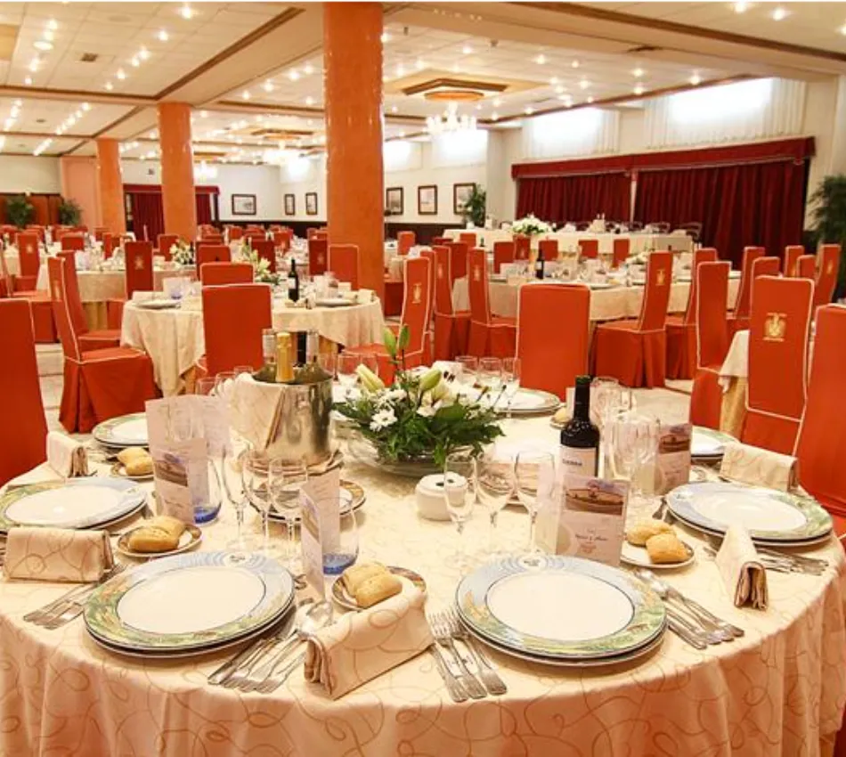 Un elegante sal&oacute;n de banquetes con mesas redondas y sillas rojas, decorado para un evento formal.