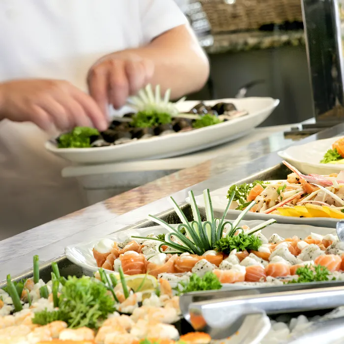 Plato de mariscos con decoraci&oacute;n de vegetales, chef preparando el emplatado al fondo.