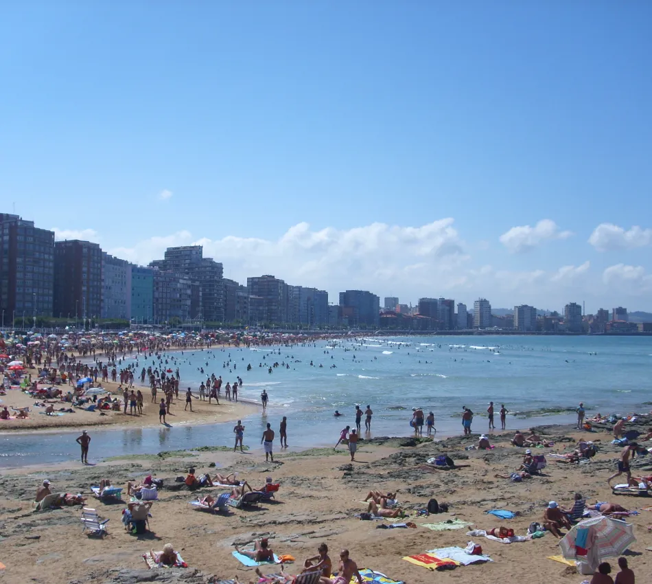 Playa concurrida con edificios altos y cielo despejado en el fondo.
