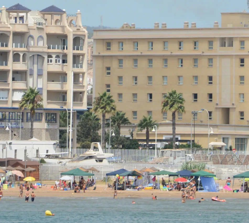 Edificios junto a una playa concurrida con sombrillas y ba&ntilde;istas en el agua.