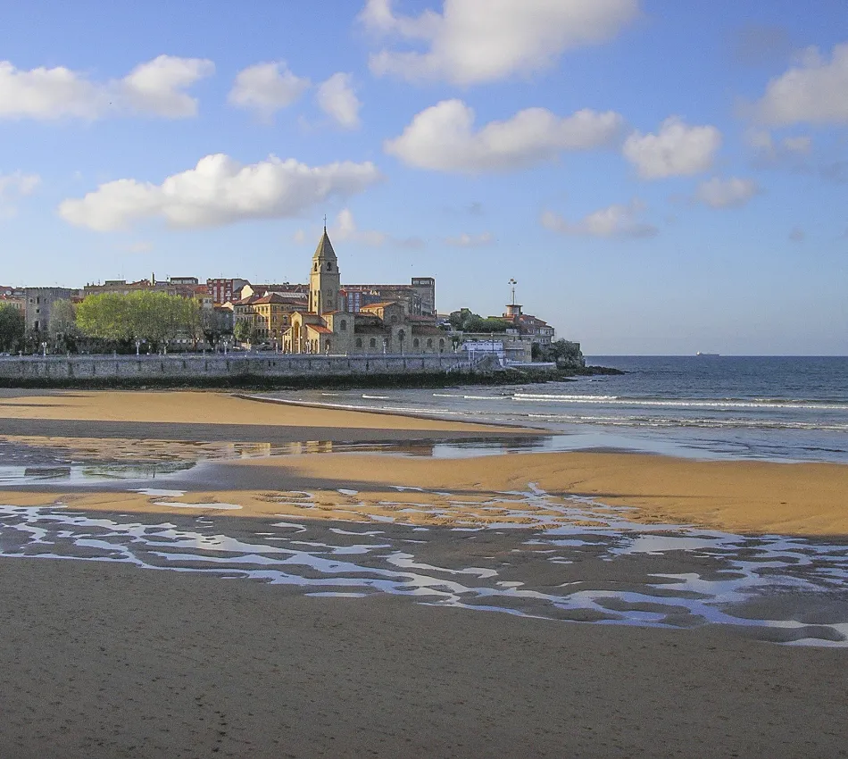 Playa con vistas a una iglesia y edificios al fondo, cielo azul con nubes dispersas.