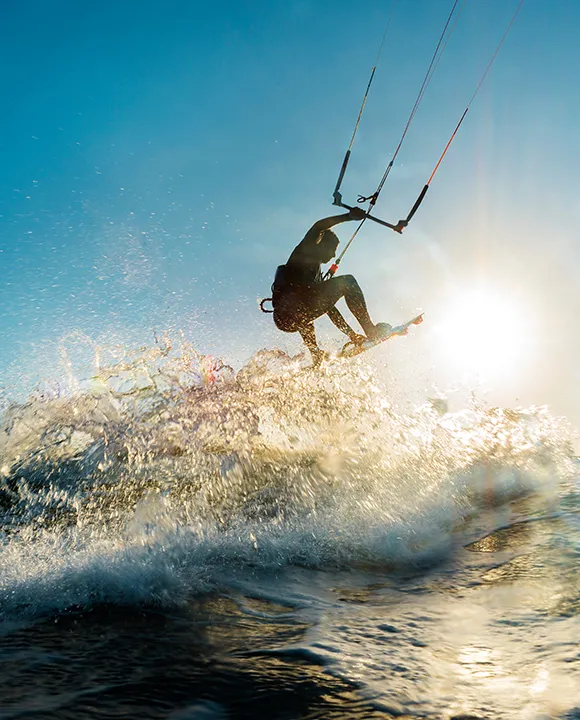 Persona haciendo kitesurf sobre olas con el sol al fondo.
