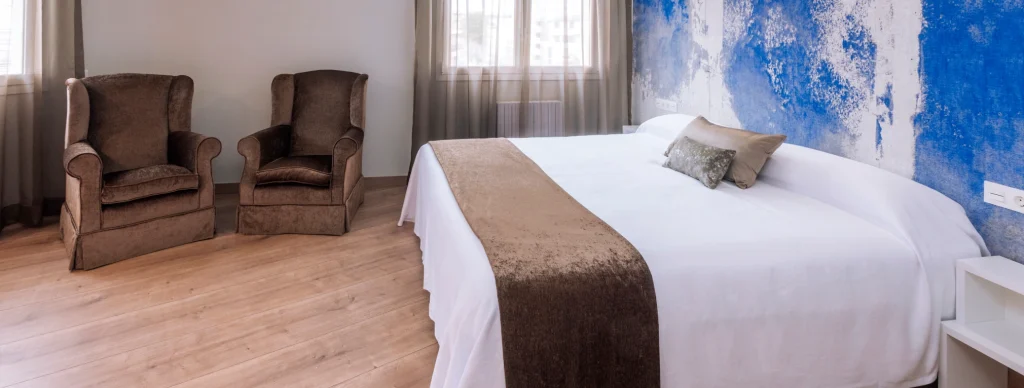 Habitaci&oacute;n con dos sillones, cama grande y pared azul decorativa.