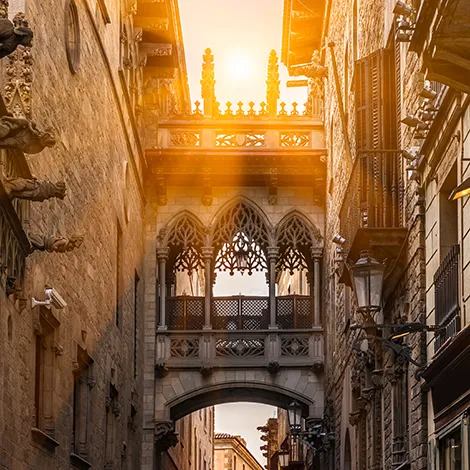 Calle estrecha con arco g&oacute;tico y luz solar al fondo en una ciudad hist&oacute;rica.