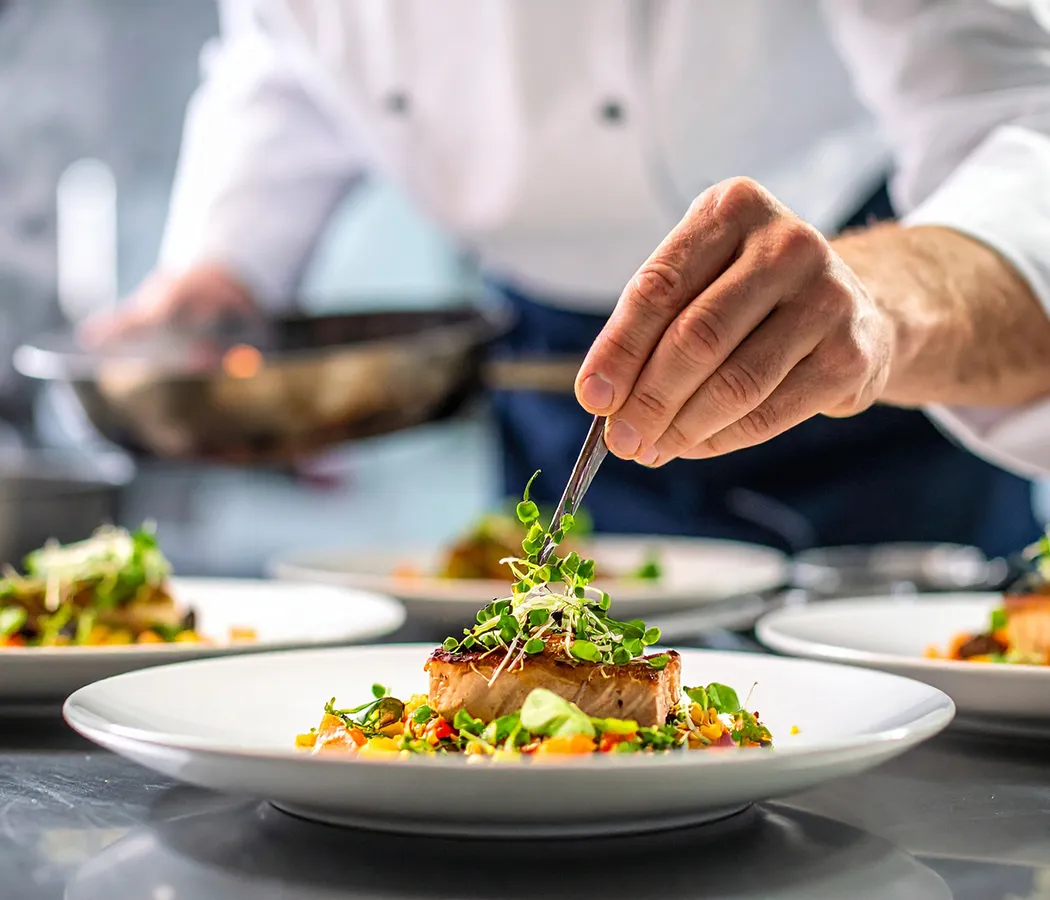 Chef decorando un plato gourmet con pinzas en la cocina.