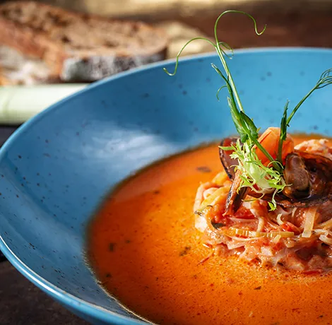 Plato de pasta en salsa roja servido en un cuenco azul con decoraci&oacute;n verde.