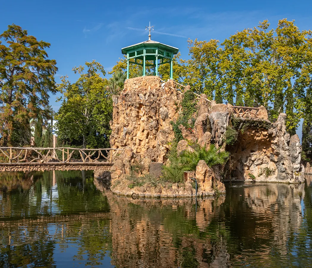 Mirador en rocas rodeado de agua y &aacute;rboles bajo un cielo azul.