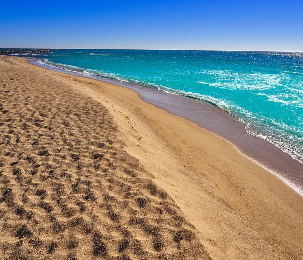 Playa con arena dorada y mar azul bajo un cielo despejado.