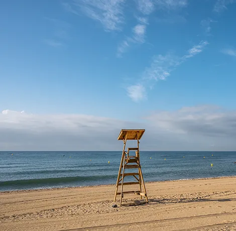 Torre de vigilancia en playa desierta bajo cielo azul y nubes.