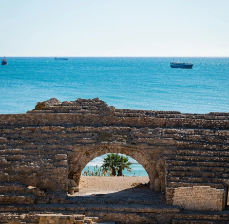 Ruinas antiguas con vista al mar y barcos en el horizonte.