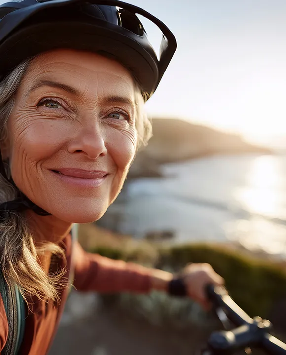 Mujer en bicicleta sonr&iacute;e junto al mar en una soleada tarde.