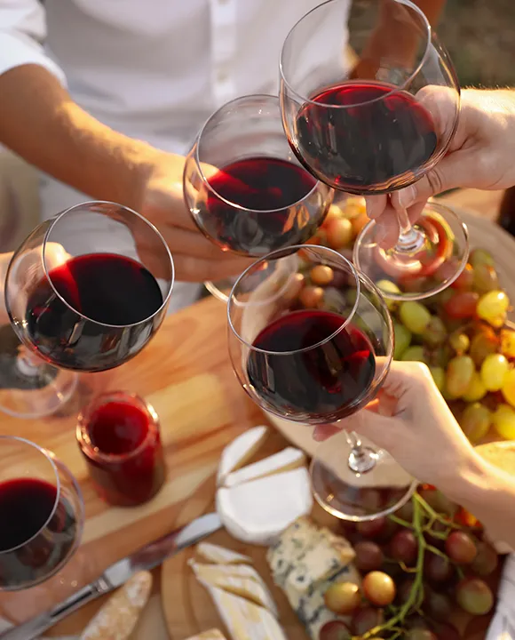 Brindis con copas de vino tinto junto a una tabla de quesos y uvas.