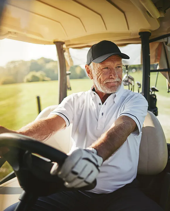 Hombre conduciendo un carrito de golf en un campo verde.