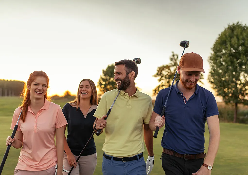 Cuatro personas sonr&iacute;en juntas en un campo de golf al atardecer.