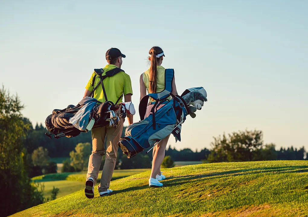 Dos personas caminan en un campo de golf llevando bolsas de palos.