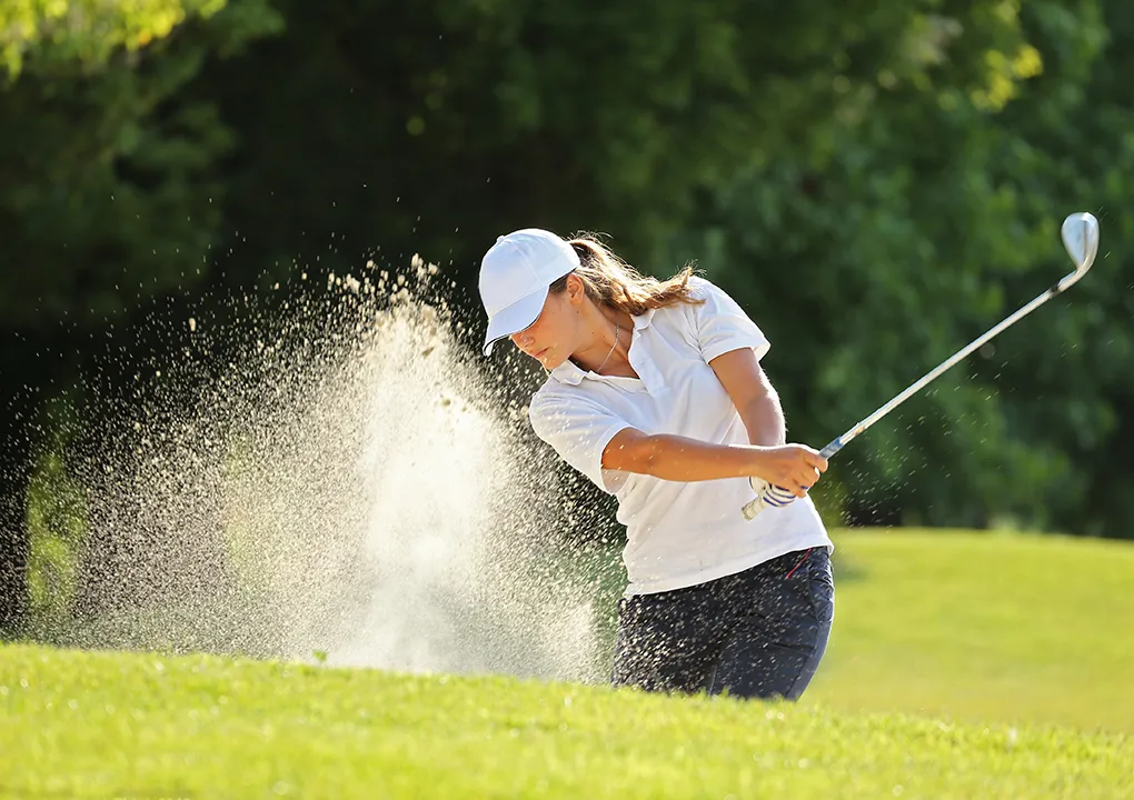 Mujer jugando golf en un campo, en posici&oacute;n de golpeo.