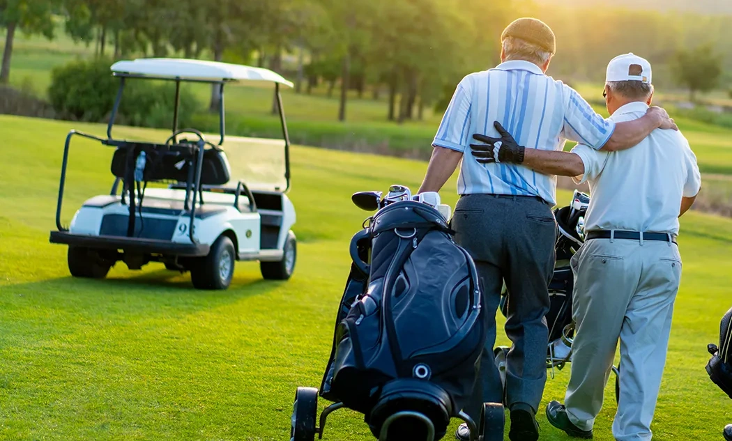 Dos personas mayores caminan abrazadas en un campo de golf al atardecer.