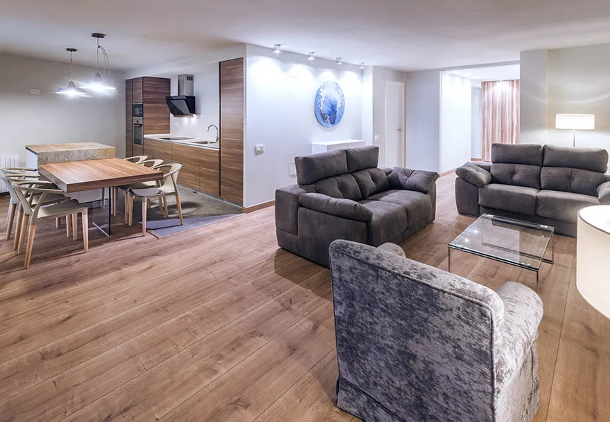 Sala moderna con sof&aacute;s grises, mesa de comedor y cocina integrada.