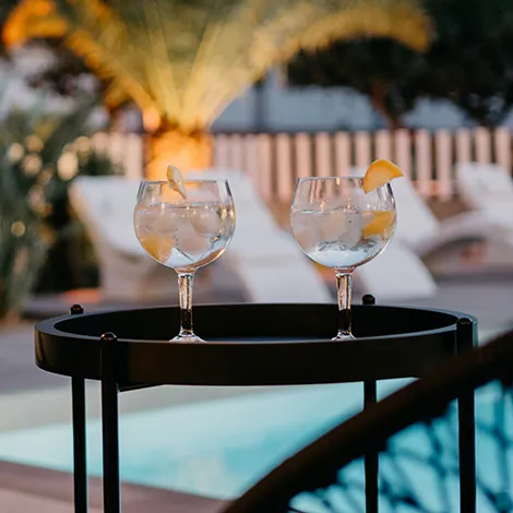 Dos copas de c&oacute;ctel en una mesa cerca de una piscina al aire libre.