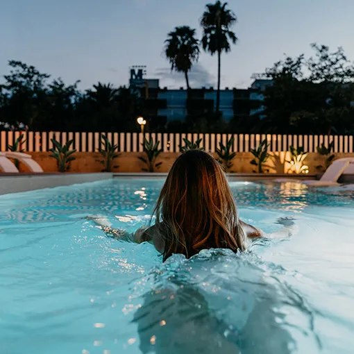 Persona nadando en una piscina al atardecer, rodeada de naturaleza.