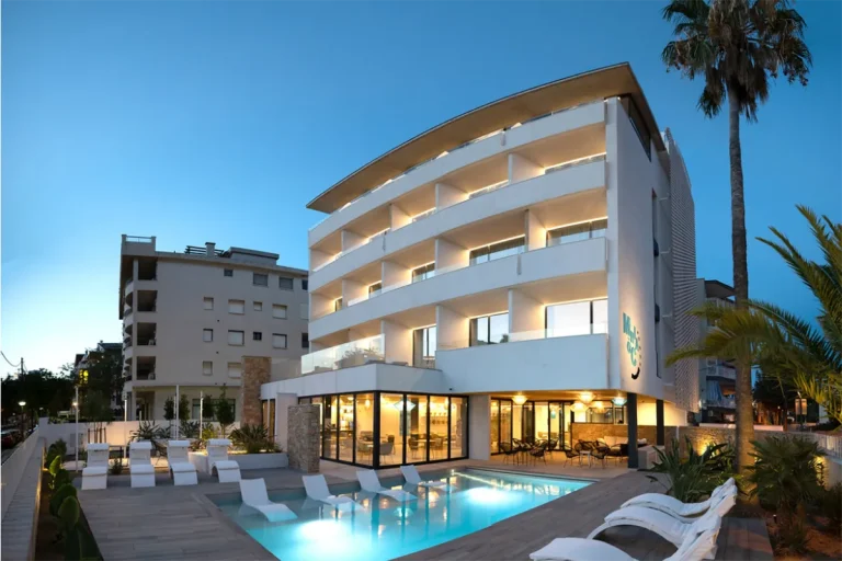 Edificio moderno iluminado, con piscina al atardecer.