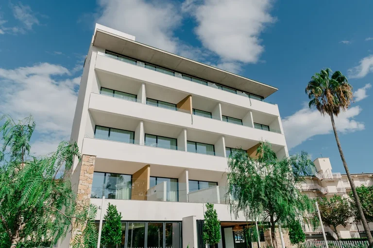 Edificio moderno de cinco pisos rodeado de palmeras y cielo azul.