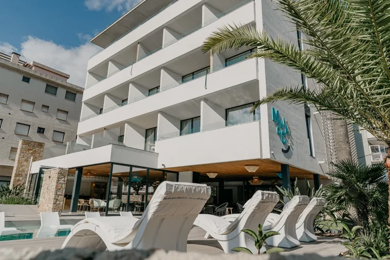 Hotel moderno con balcones y tumbonas junto a una piscina al aire libre.