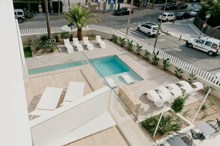 Piscina moderna con sillas blancas en terraza frente a la calle.