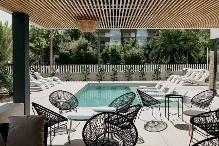 Piscina al aire libre con tumbonas y sillas modernas bajo p&eacute;rgola de madera.