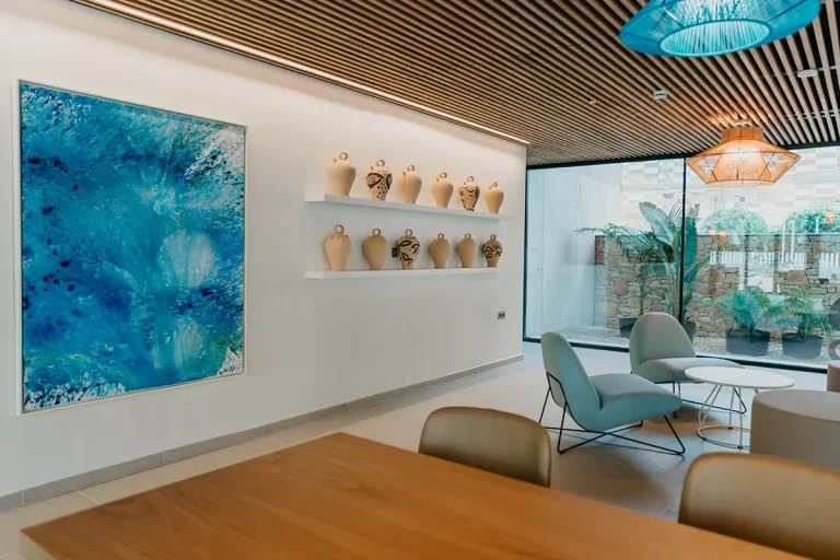 Sala moderna con sillas azules, jarrones y cuadro azul abstracto en la pared.