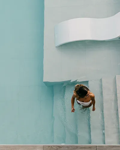 Mujer en bikini subiendo escaleras de piscina desde el agua.