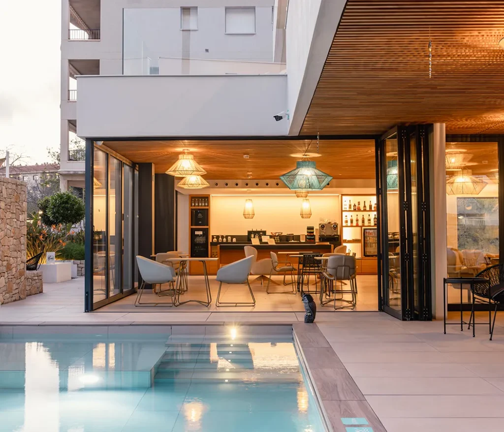 Terraza moderna con piscina, sillas y mesas, interior iluminado y elegante.