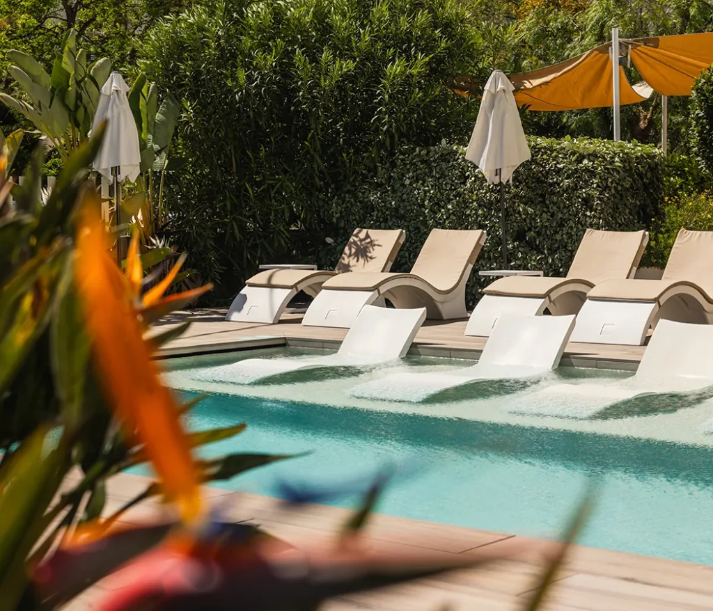 Piscina con tumbonas y sombrillas rodeada de vegetaci&oacute;n.