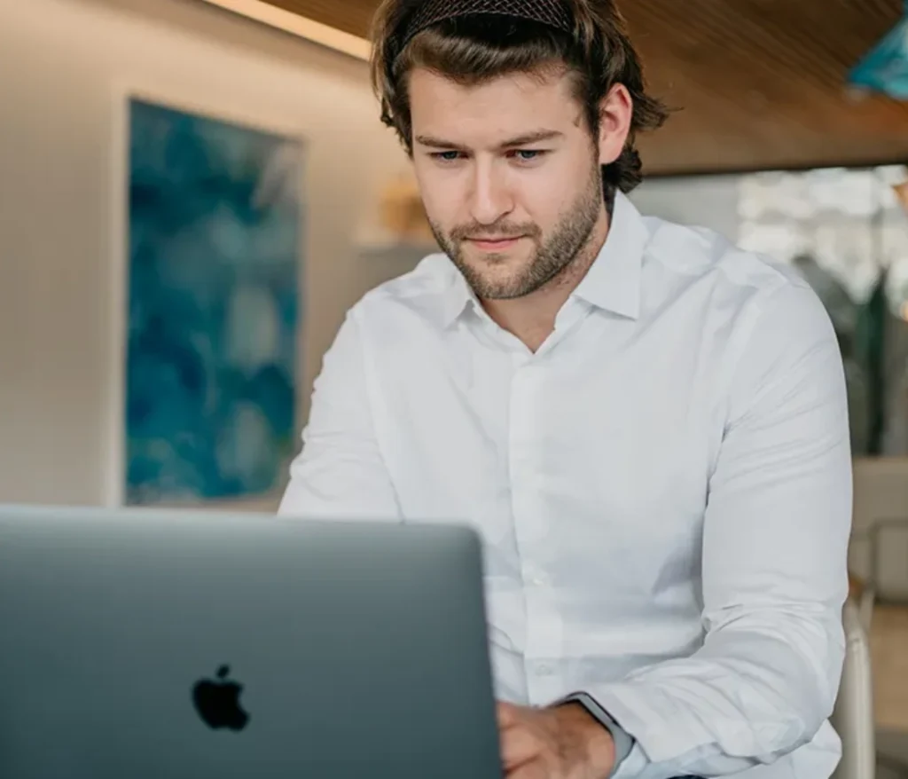 Hombre con camisa blanca trabajando en una laptop Apple.