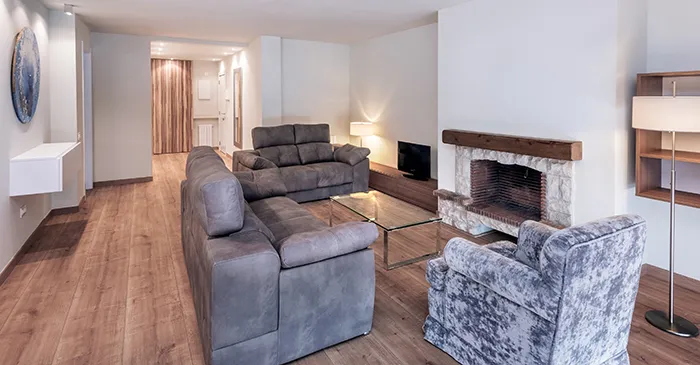 Sala moderna con sof&aacute;, sill&oacute;n y chimenea sobre piso de madera.