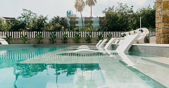 Piscina con sillas sumergidas y vegetaci&oacute;n de fondo.