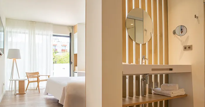 Habitaci&oacute;n luminosa con cama, silla, lavabo y ventana.