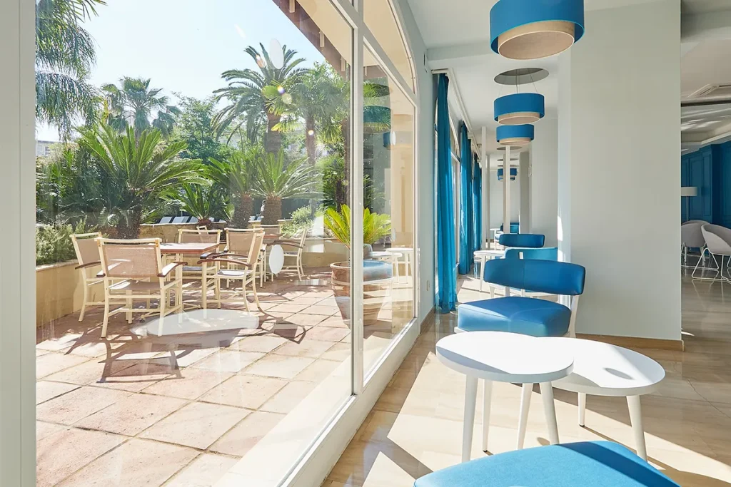 Sala interior luminosa con sillas azules, vista al jard&iacute;n con palmeras.